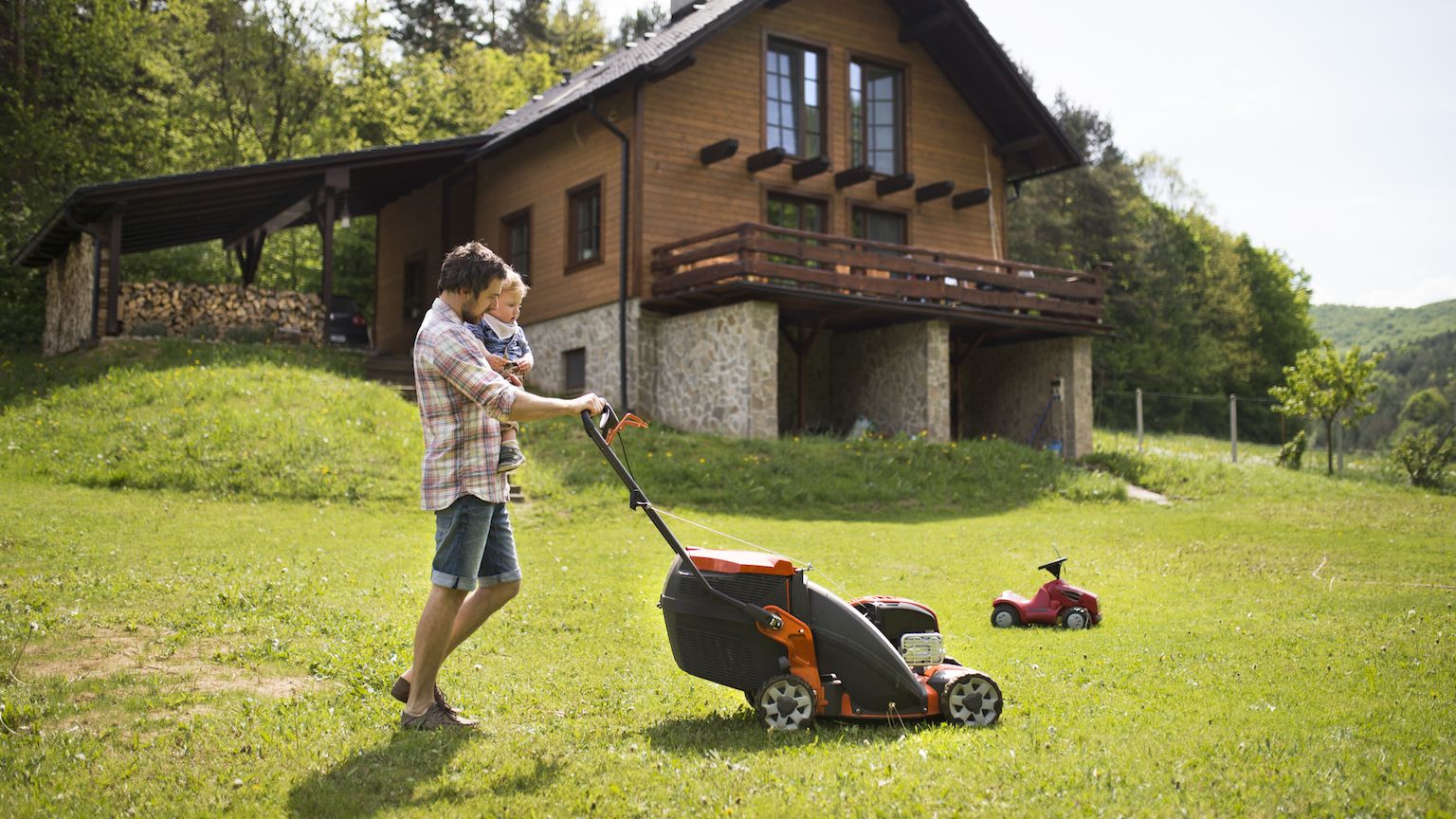 Man moving the lawn while holding his son.
